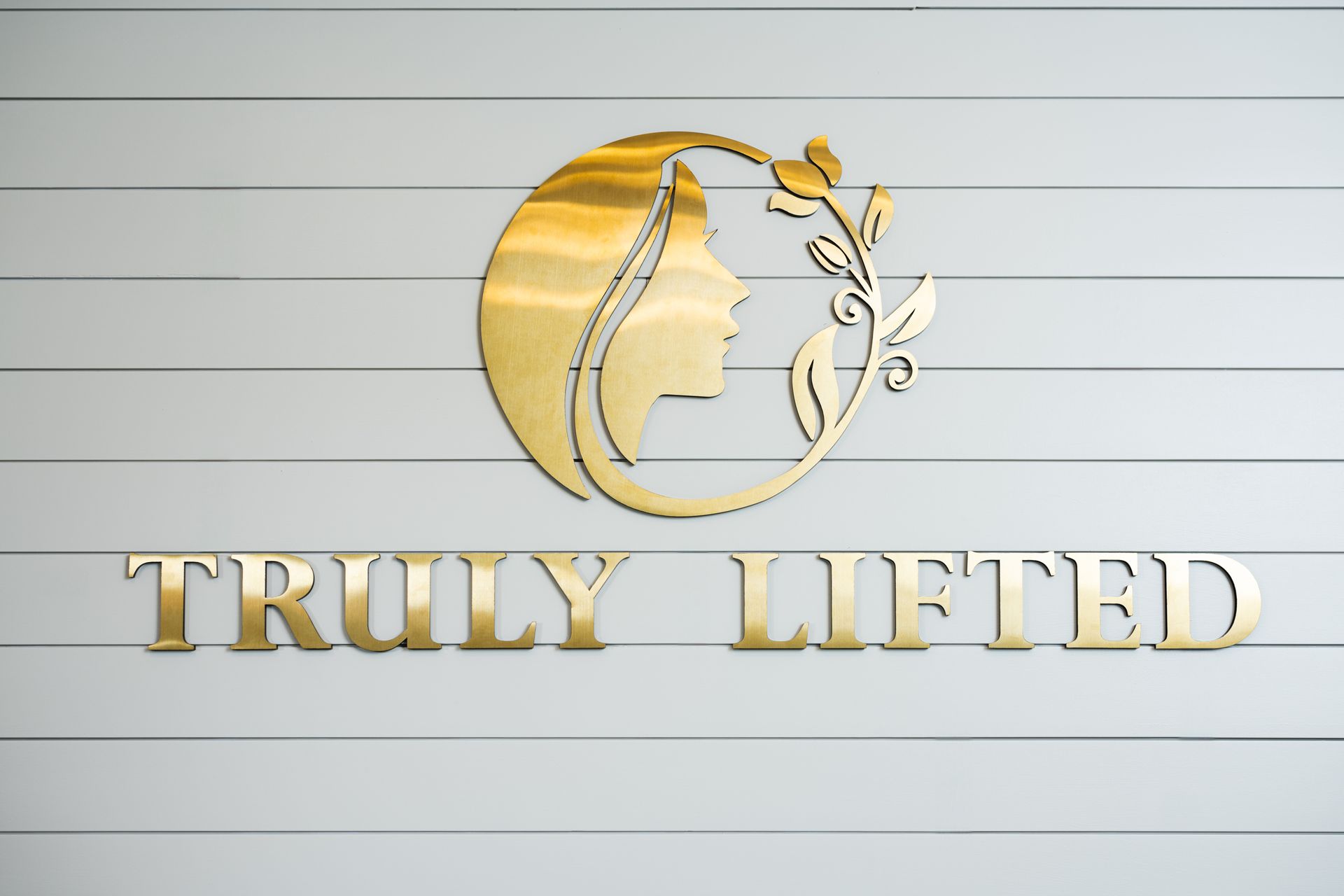 Gold “Truly Lifted” logo with a woman’s profile and leafy design on a light striped background