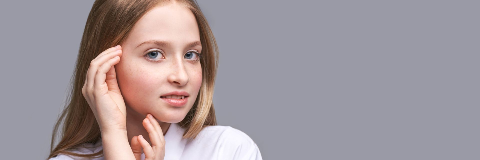 Portrait of a person with long hair touching their ear against a gray background