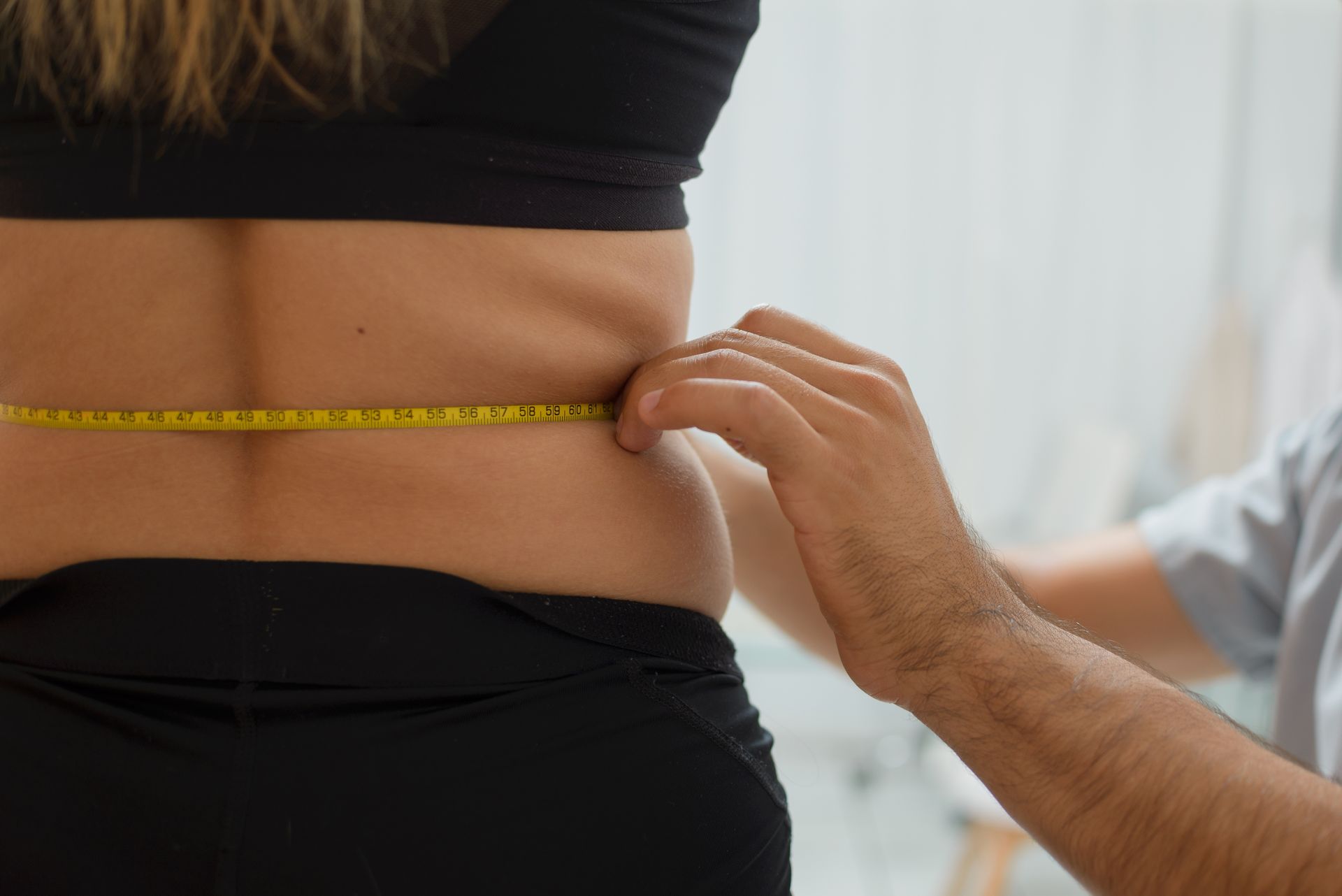 A person measures another person’s waist with a yellow tape measure.