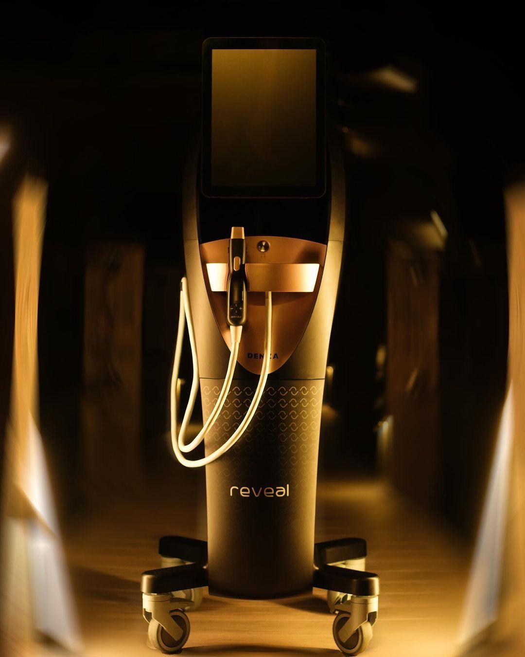 Black Reveal laser skin tightening machine with a touchscreen and attached treatment devices, on wheels.