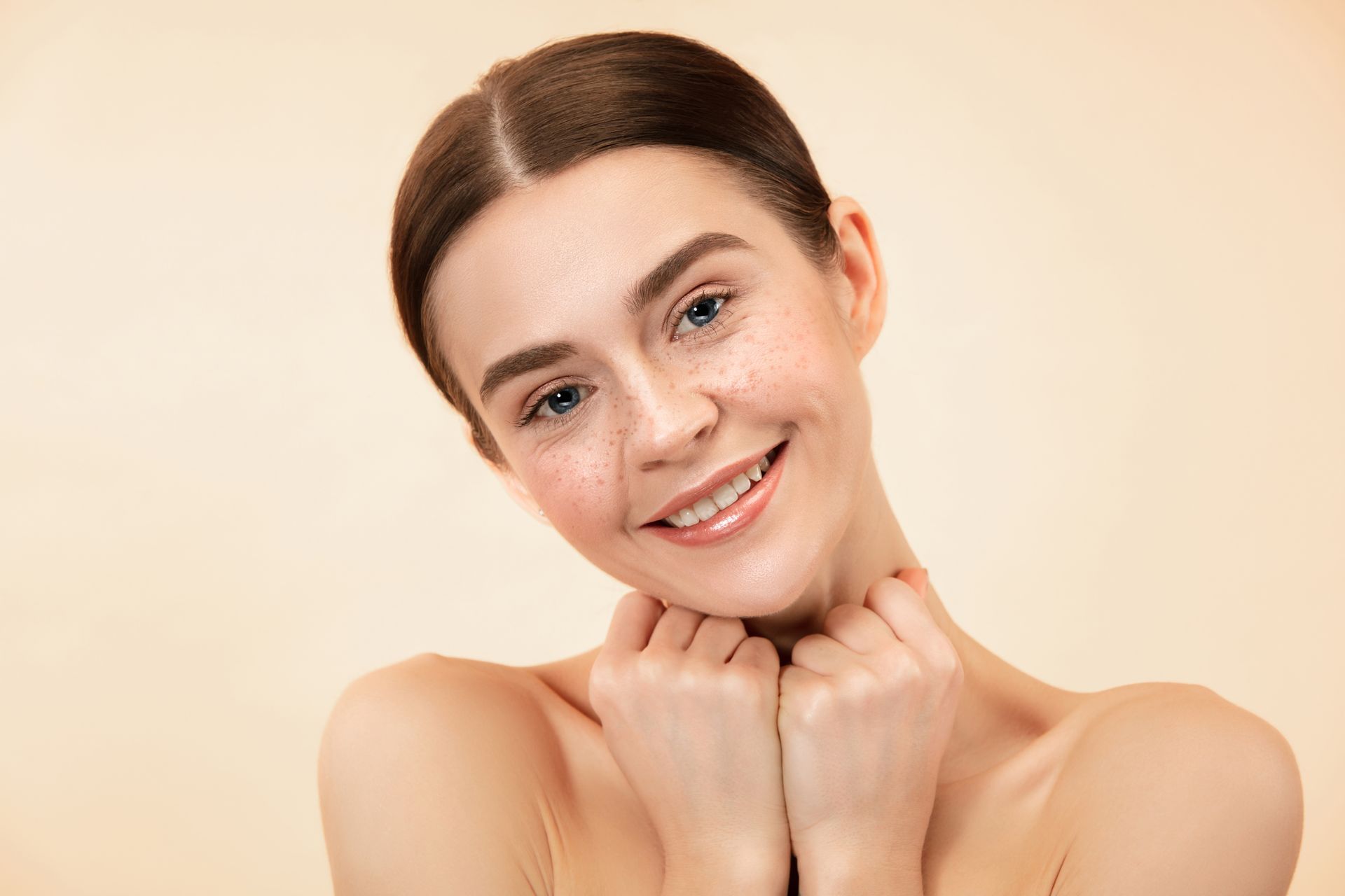 a woman with freckles on her face is smiling and touching her neck .