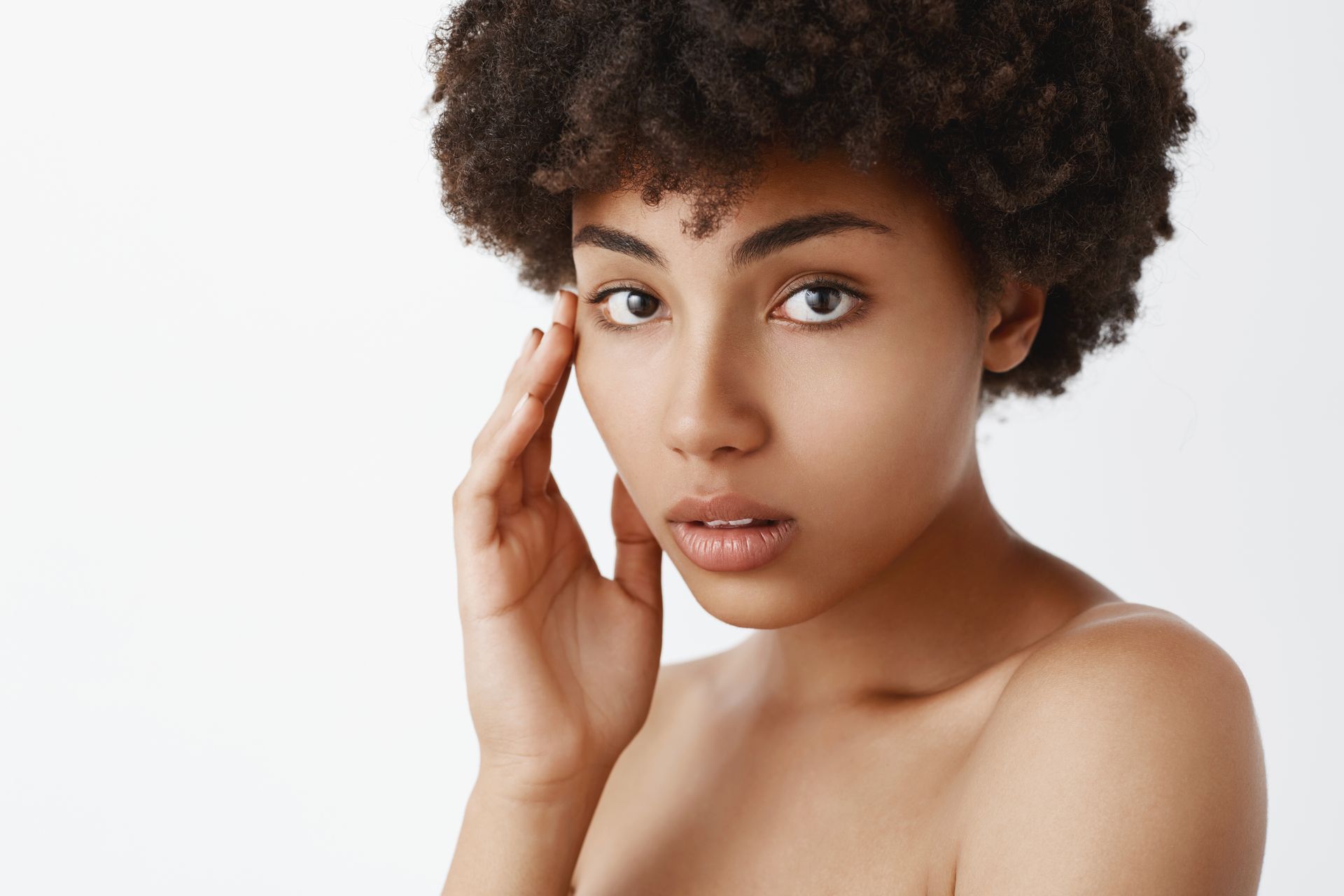 a woman with curly hair is touching her face with her hand .