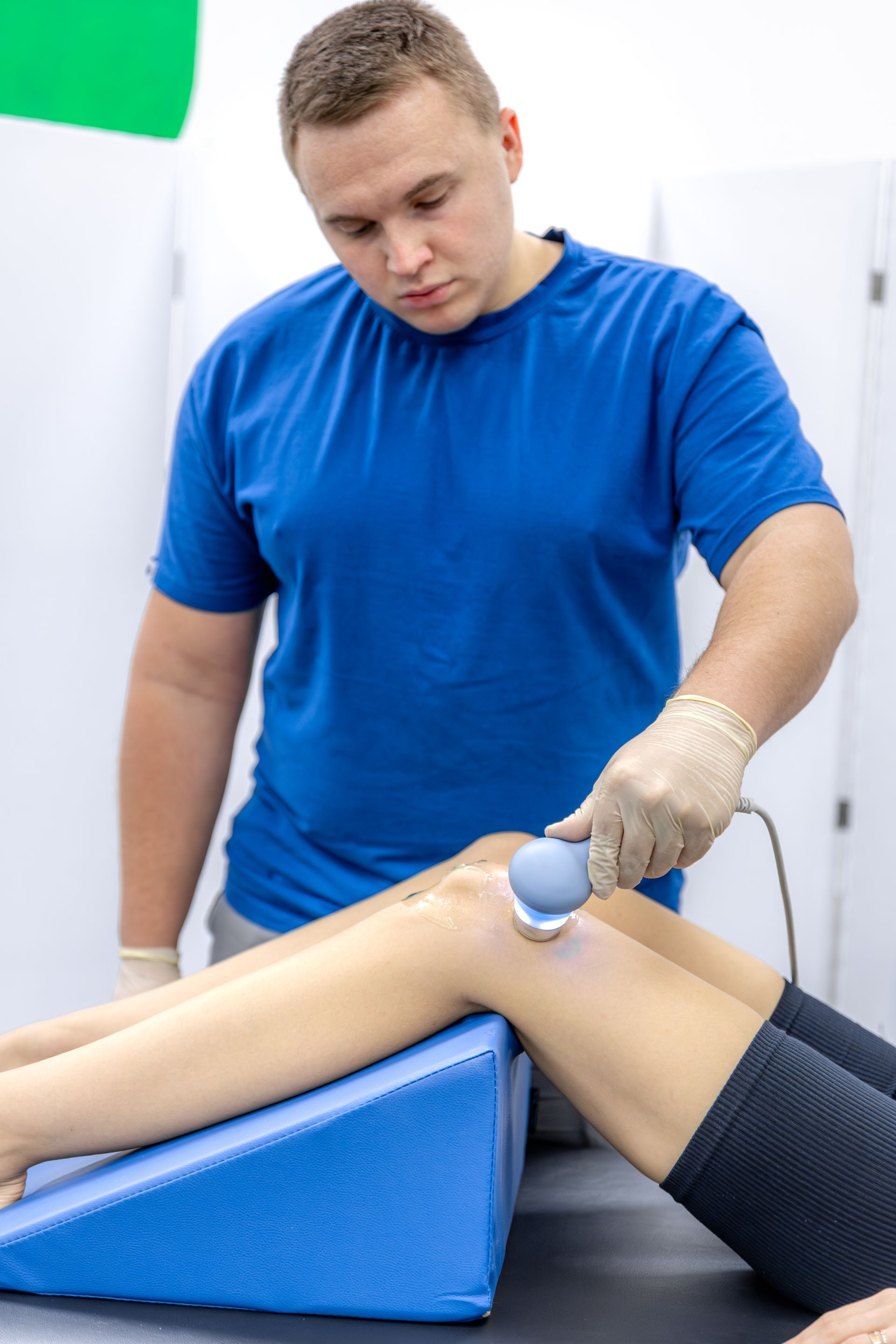 Physical therapist using a handheld device on a patient's bent knee during leg treatment