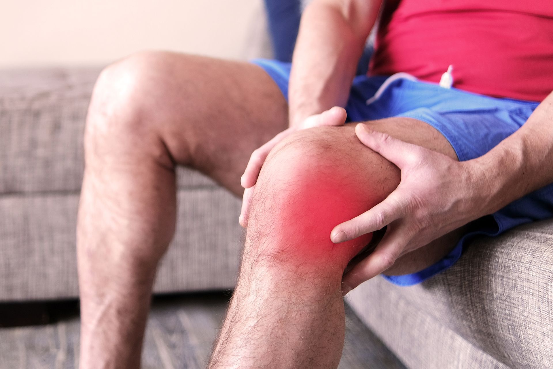 Person holding a red, painful-looking knee while sitting on a couch