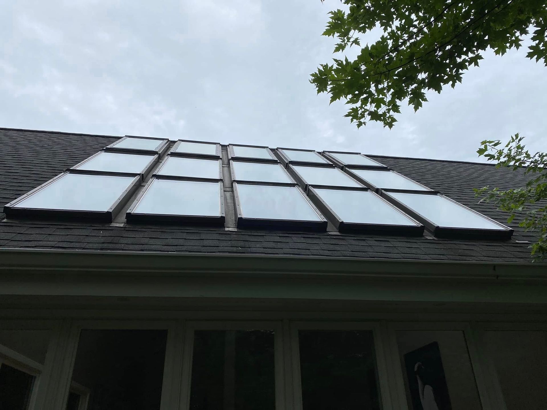 Roof with solar panels viewed from below against a cloudy sky, with tree branches framing the top right.