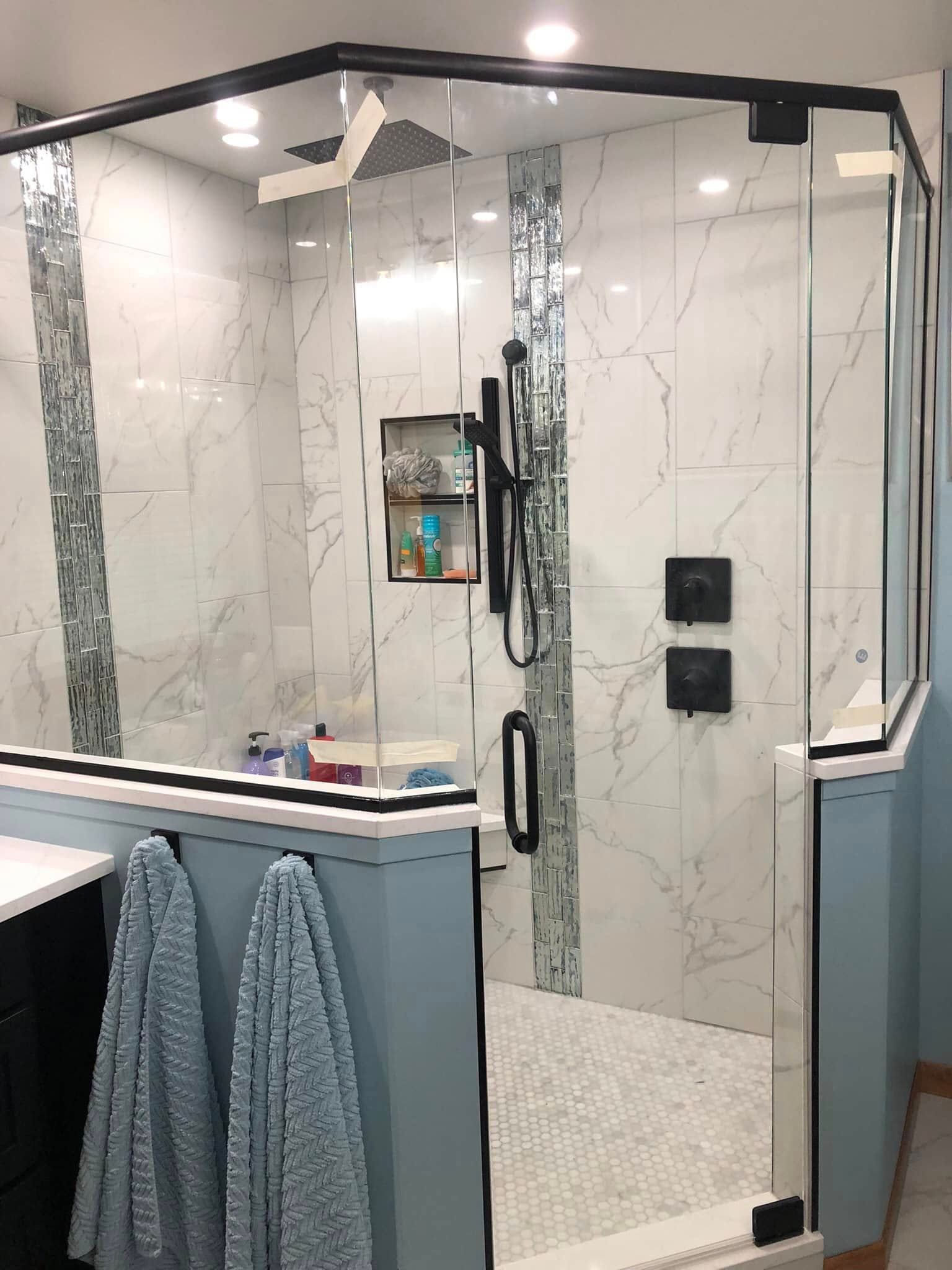 Modern shower with glass enclosure, marble-look tile, handheld shower, and blue towels hanging outside the door