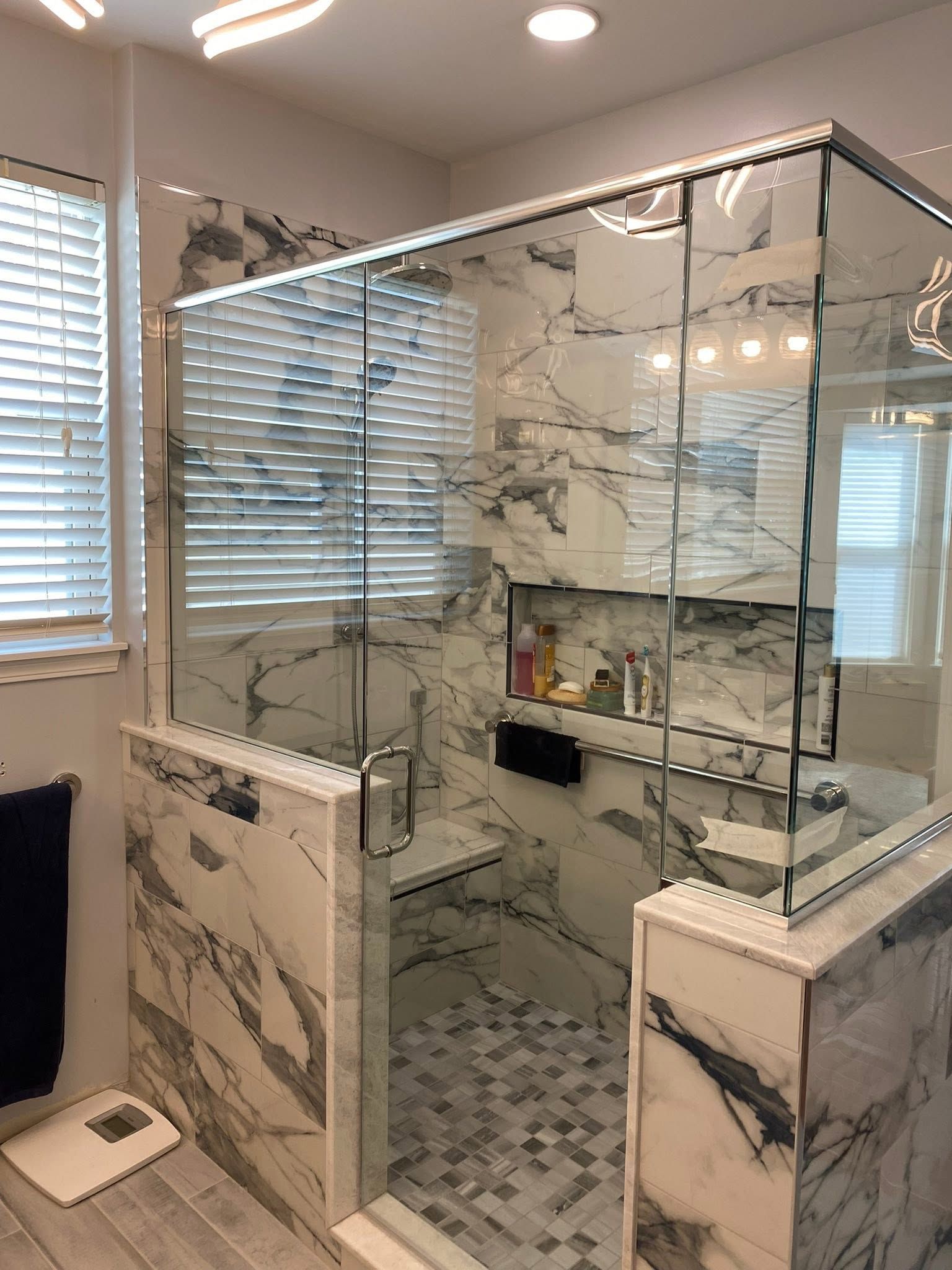 Marble-tiled glass shower enclosure with chrome frame in a bright bathroom