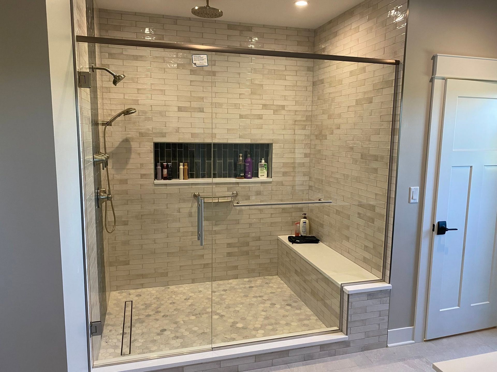 Modern walk-in tiled shower with glass door, built-in shelf, and bench in a bathroom