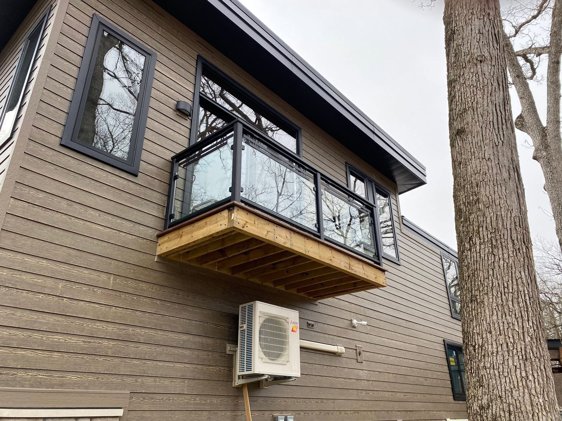 Modern house exterior with a black balcony and beige siding, plus a tree trunk in the foreground