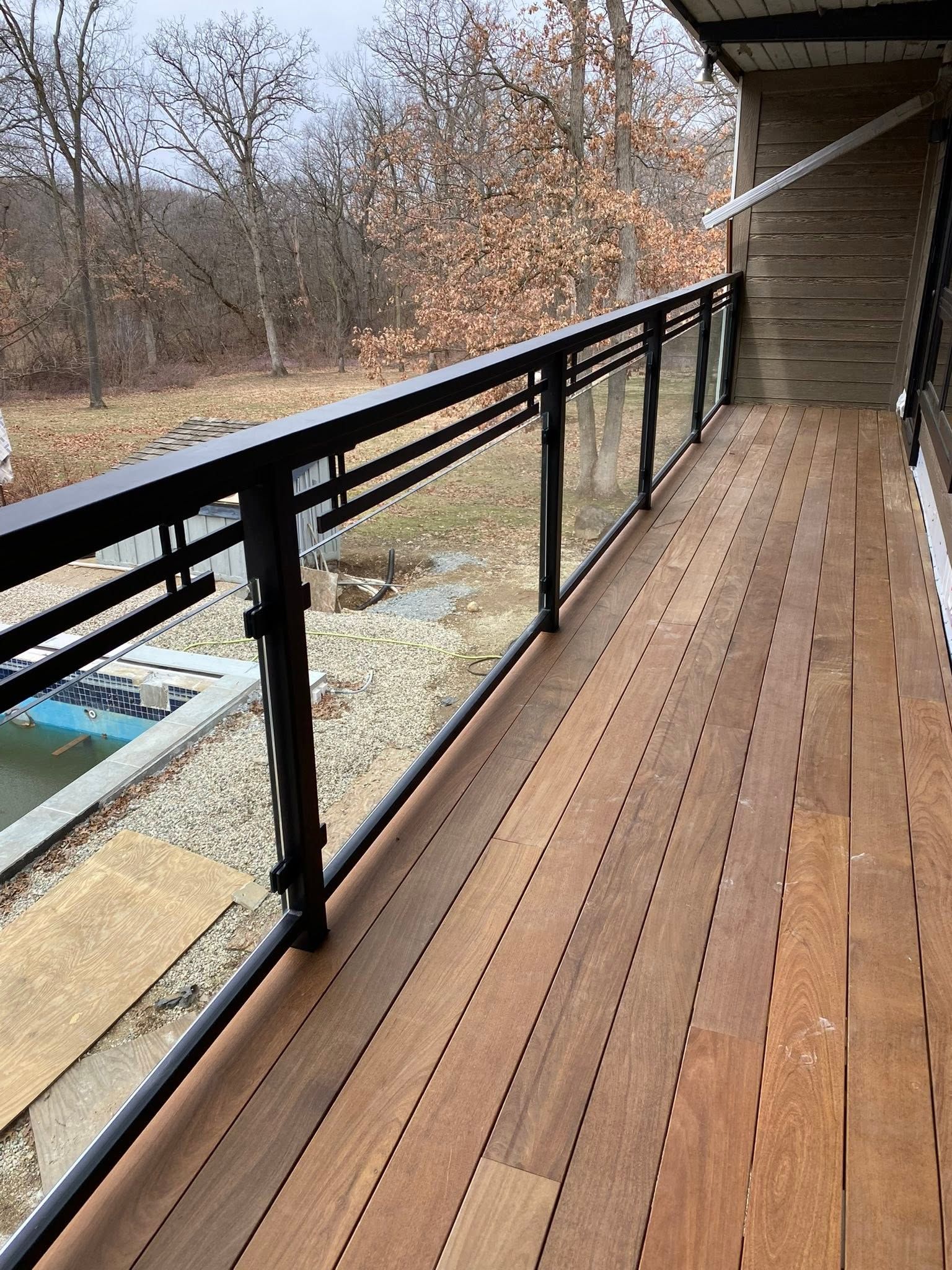 Wooden deck walkway with black railing beside a house, overlooking a wooded yard.