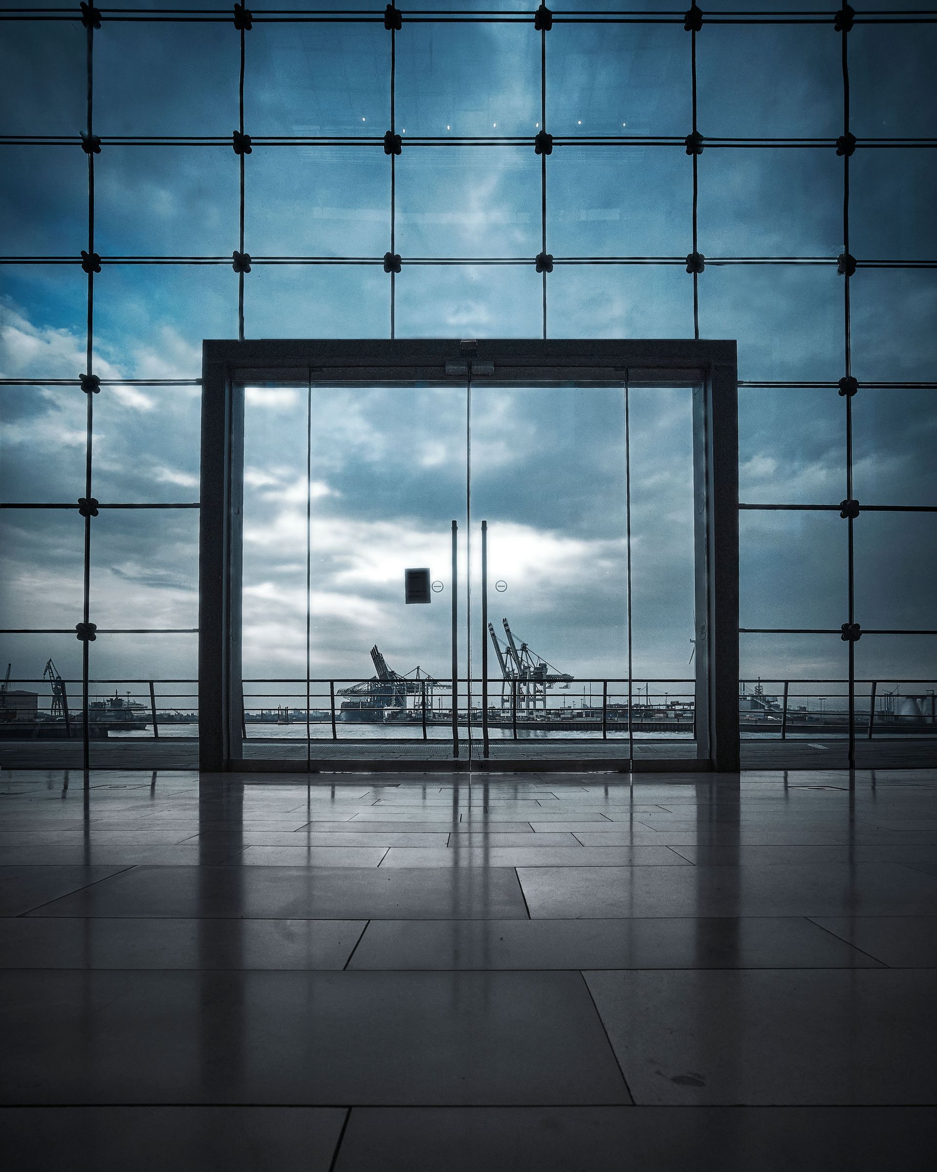 Modern glass building interior framing an airport runway and cloudy sky beyond.