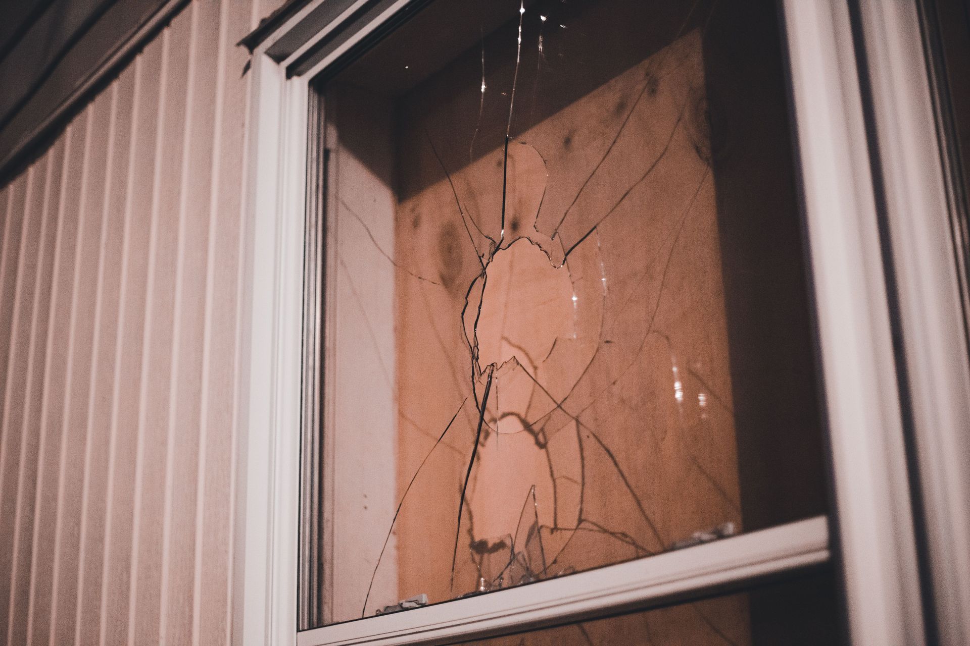 Cracked window pane in a beige framed window with white siding around it