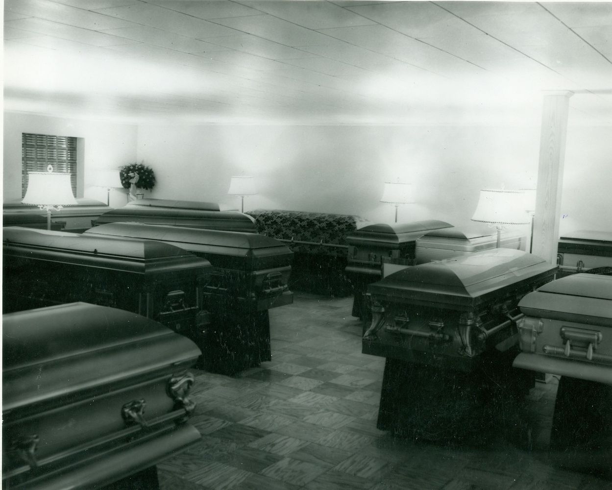 A room filled with rows of closed coffins, lit by bright windows and lamps.
