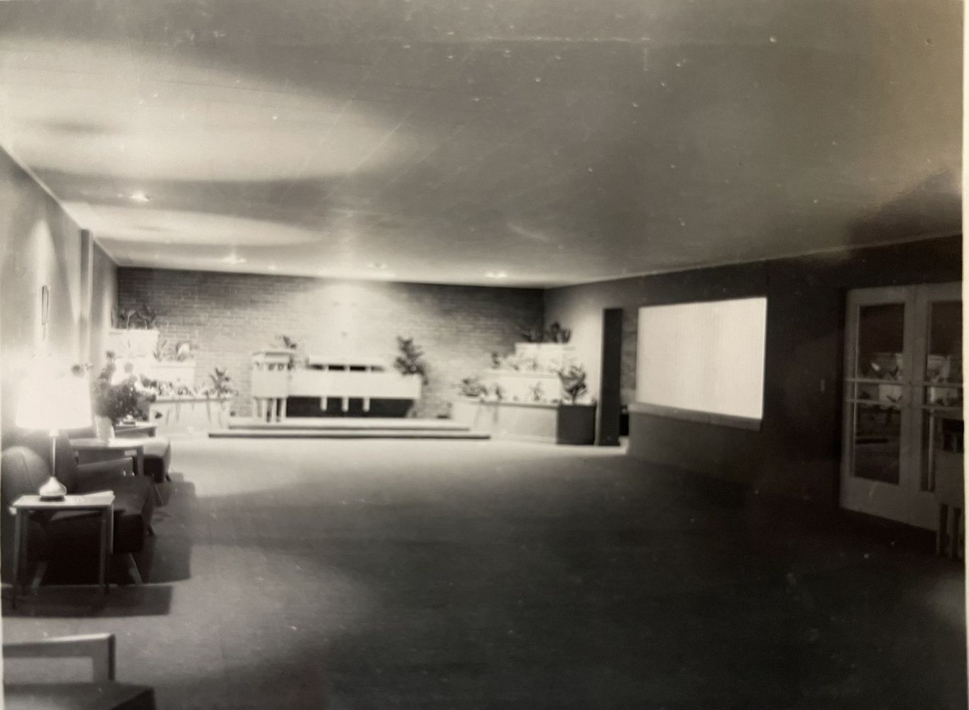 Spacious black-and-white lobby with chairs, plants, and a bright reception counter at the back.