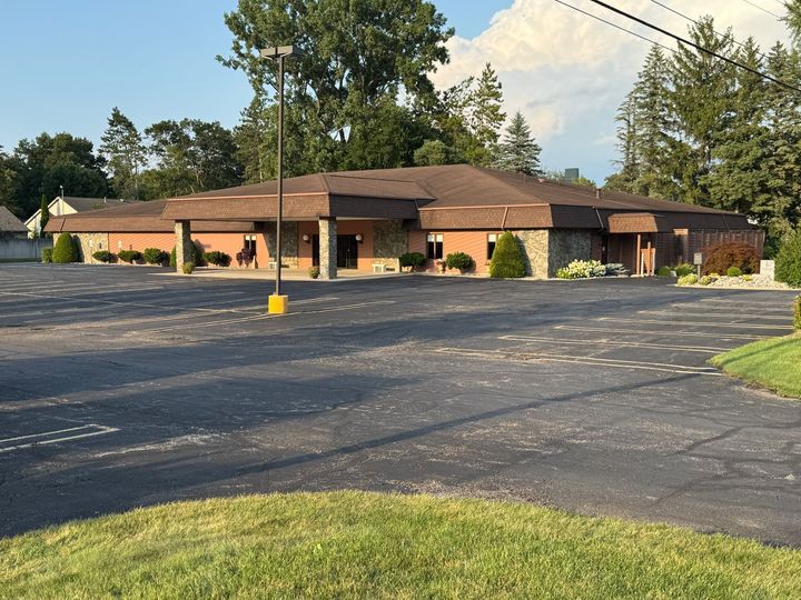 Single-story brick building with a parking lot and trees in front, under a partly cloudy sky