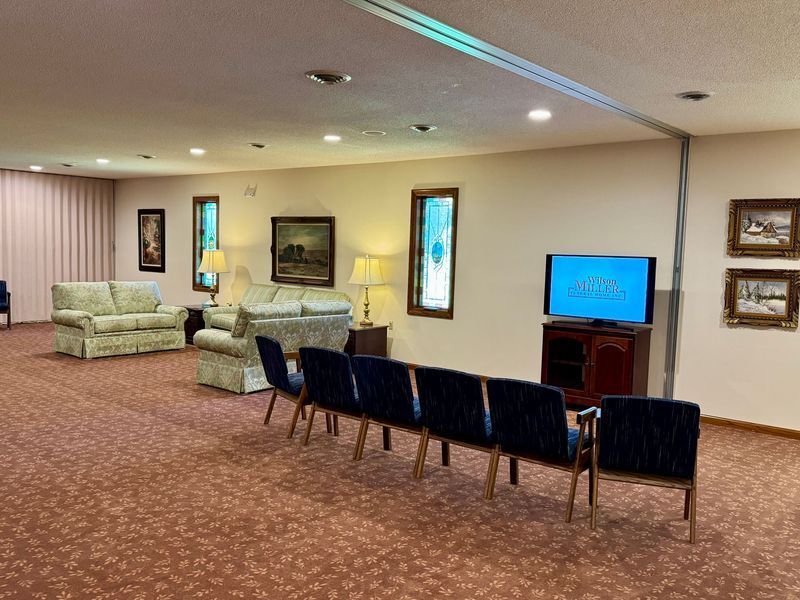 Spacious lounge with sofas, chairs, wall art, and a TV on a cabinet in a carpeted room