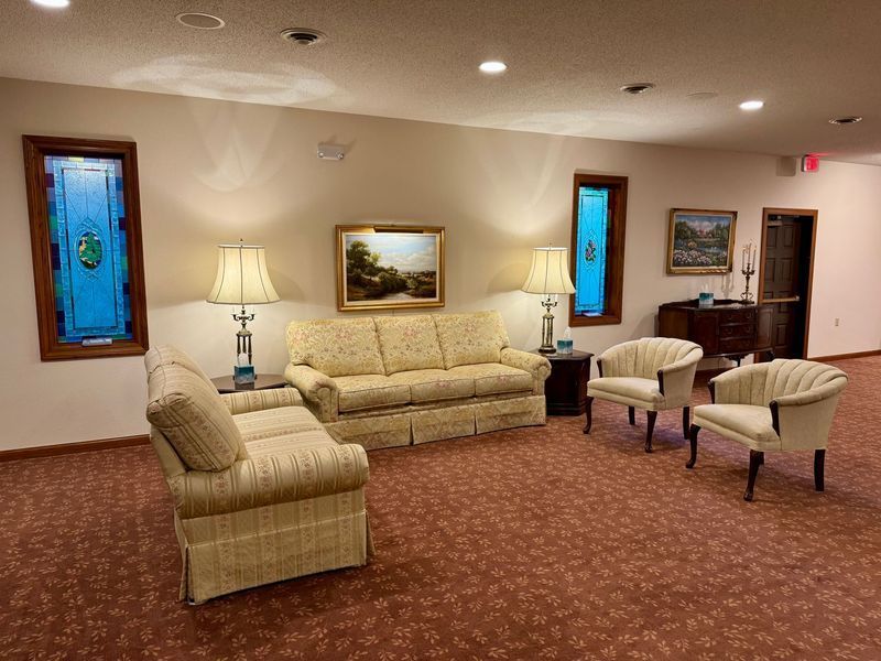 Empty waiting room with beige chairs, lamps, framed art, and patterned carpet