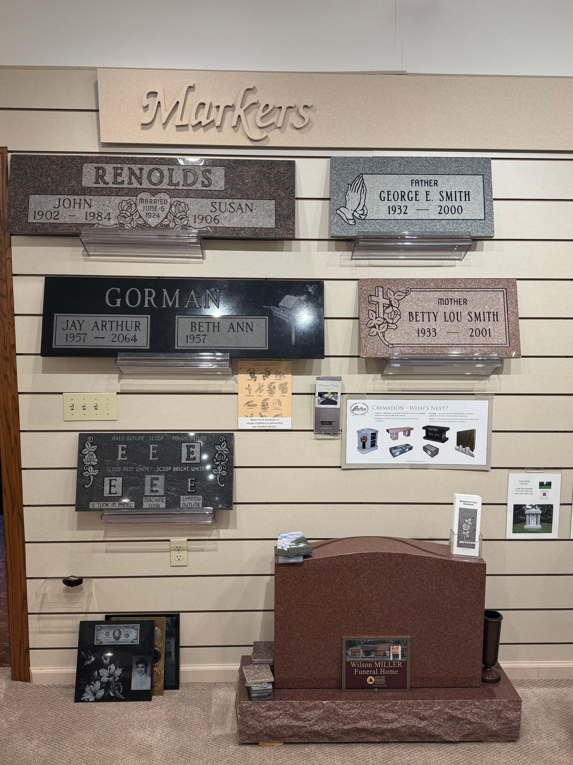 Memorial wall with engraved plaques and markers in varying colors, arranged on a beige slatwall.