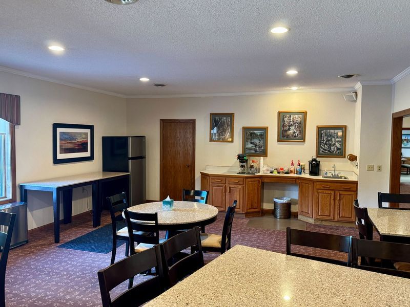 Spacious hotel breakfast room with round tables, wooden buffet cabinets, and framed wall art under recessed lights