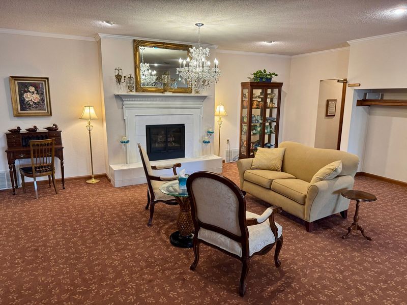 Elegant living room with fireplace, beige sofa, armchairs, chandelier, and patterned carpet