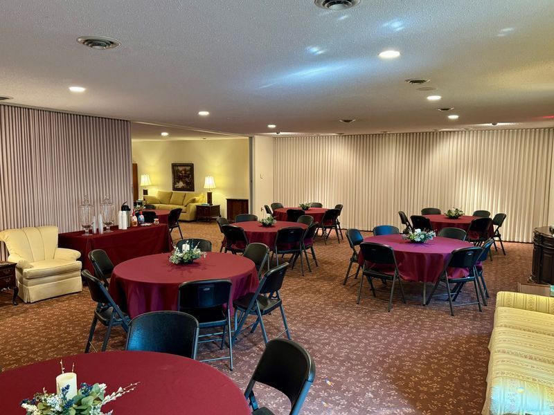 Empty banquet hall with round tables, burgundy tablecloths, black chairs, and cream curtains under soft lighting