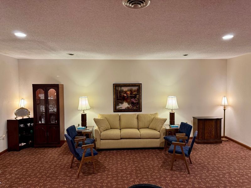 Formal lounge with beige sofa, blue chairs, lamps, and red carpet