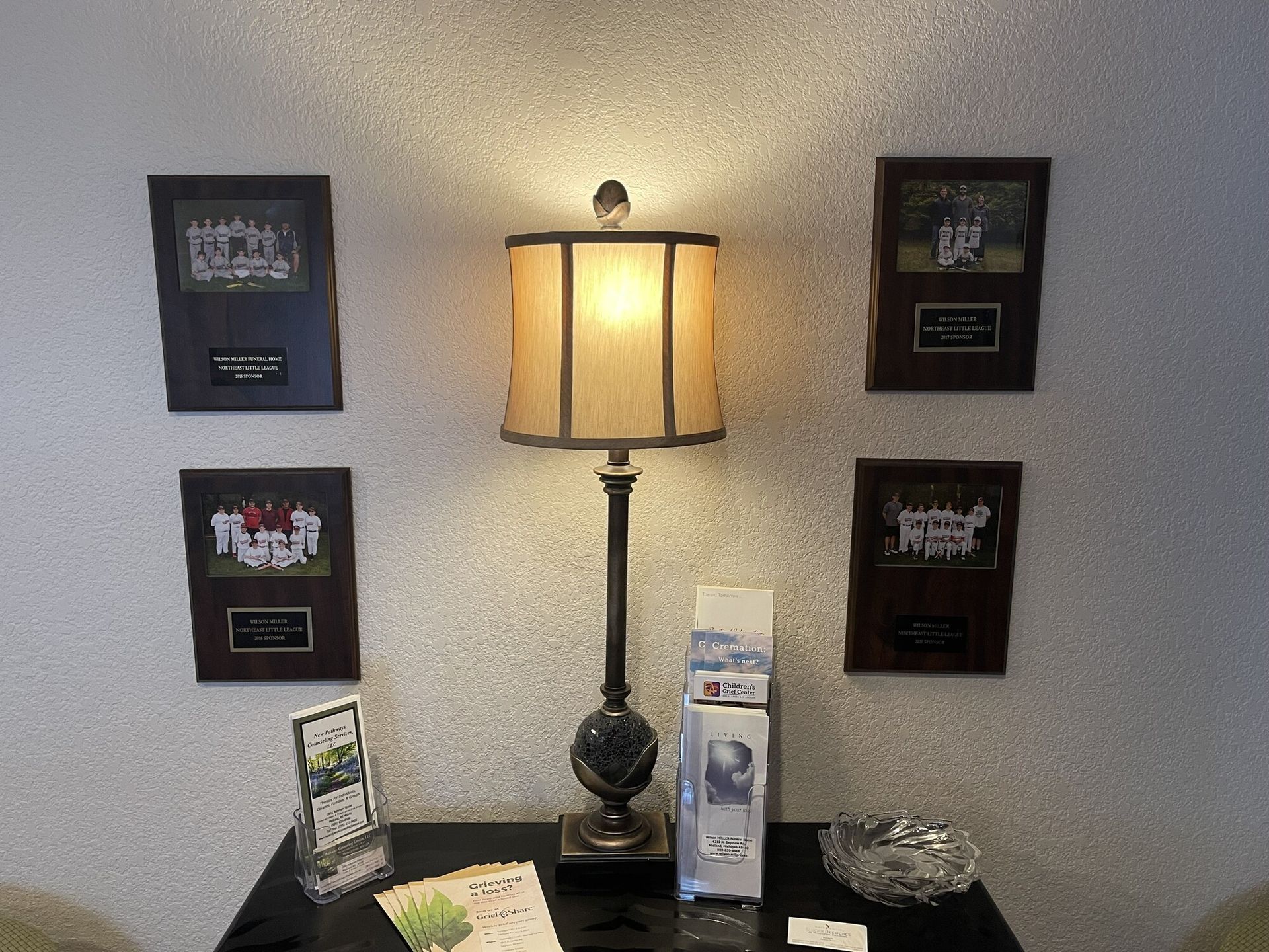 Table lamp on a console table with framed wall art and brochures on either side.
