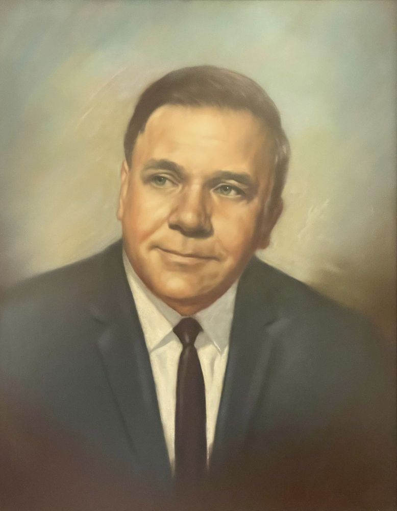 Formal portrait of a man in a dark suit and tie against a soft beige background.