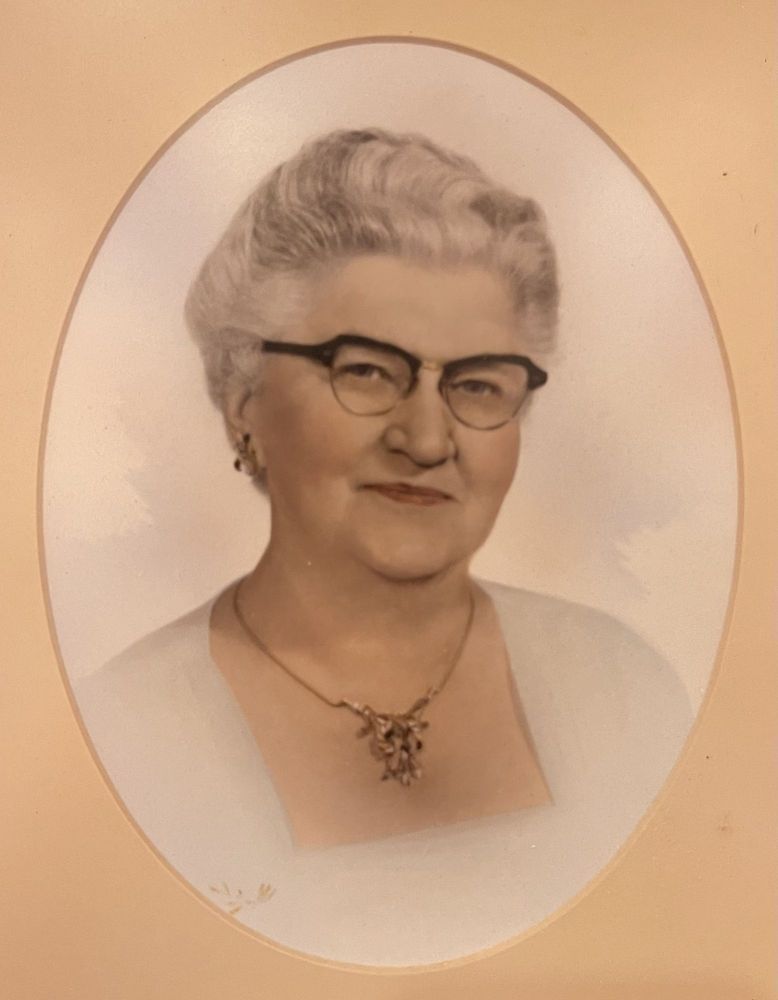 Portrait of a smiling woman with glasses and a necklace, in a soft oval frame.