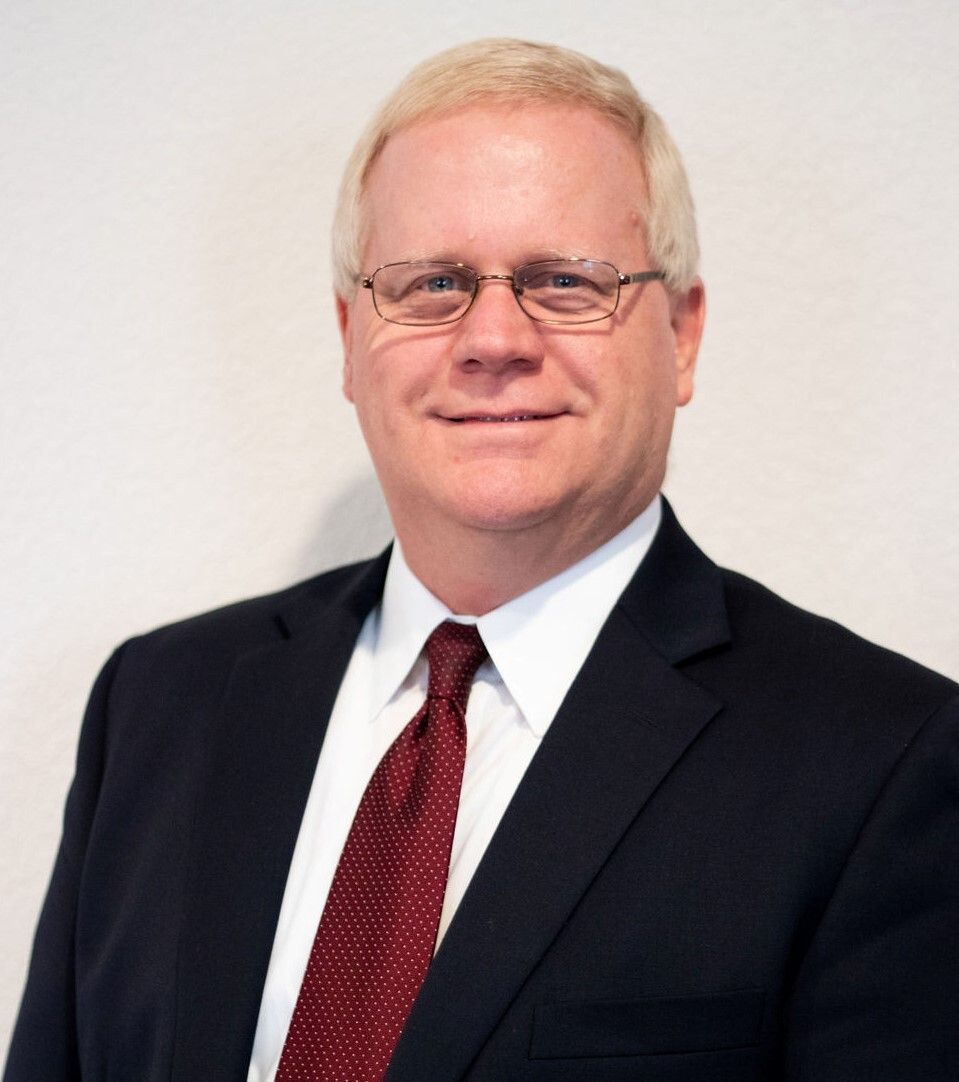Portrait of a man in a dark suit, white shirt, and red tie against a light background