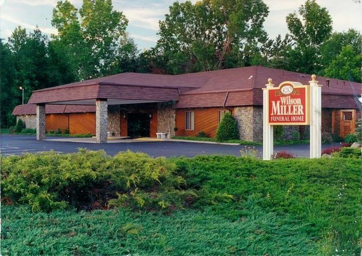 Miller restaurant building with red sign, surrounded by trees and shrubs at dusk