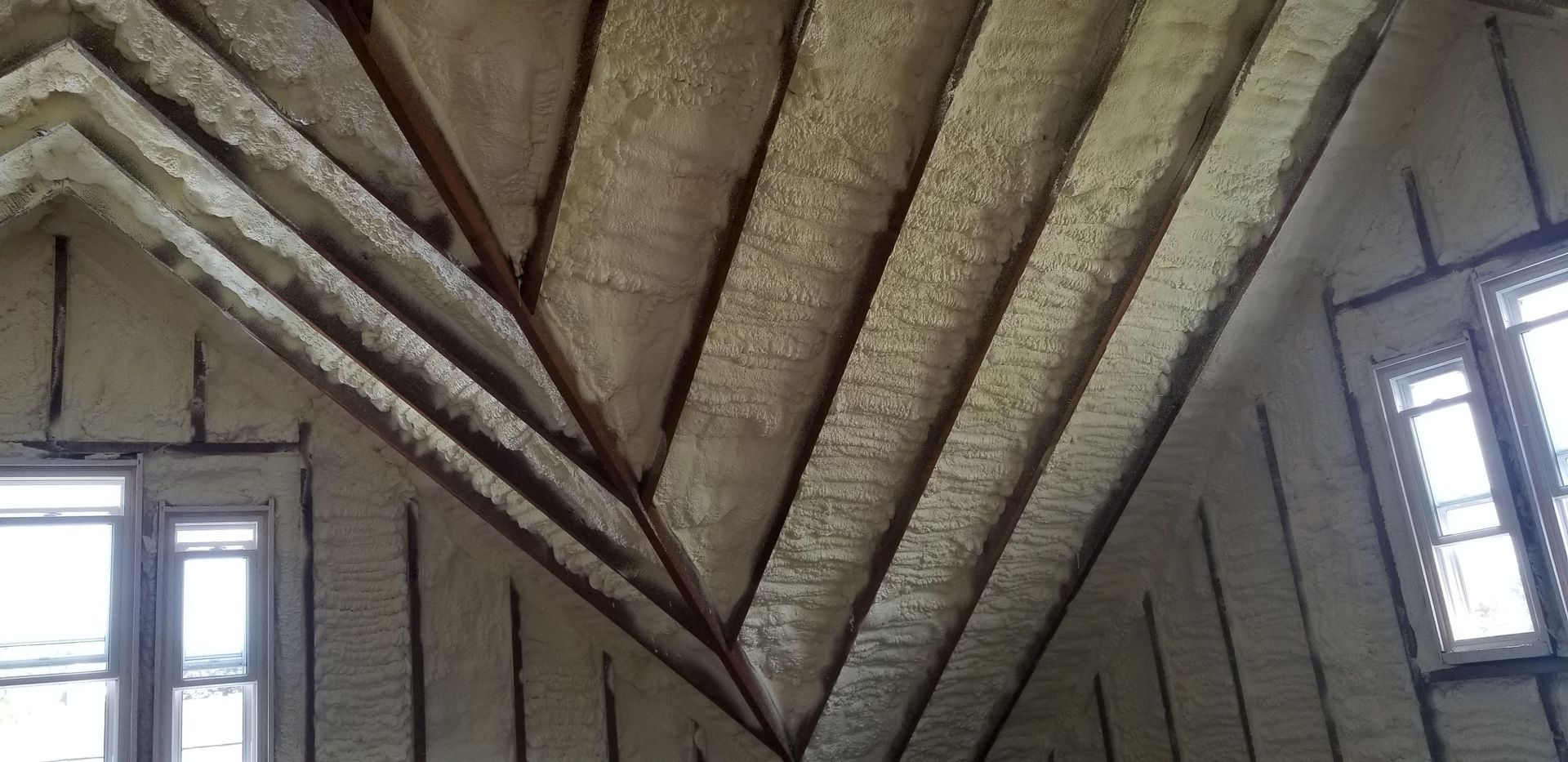 Insulated attic ceiling with exposed beams and two windows on either side