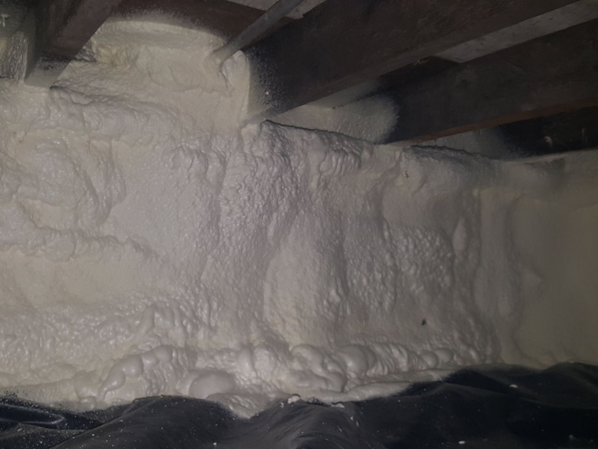 Foam insulation sprayed between wooden beams in an unfinished attic space