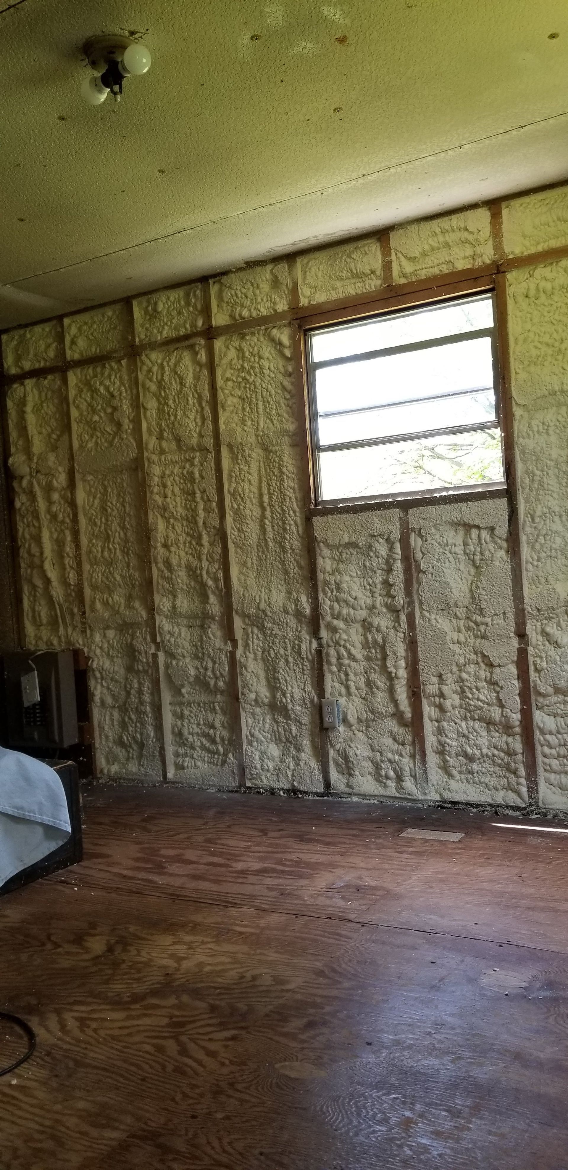 Sparse room with worn wood floor, patterned walls, and a barred window.