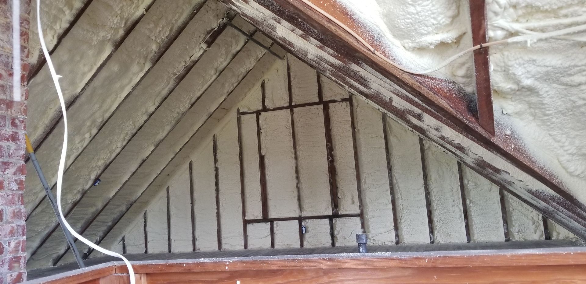 Triangular attic wall with exposed wooden beams and a small barred opening under a brick roof