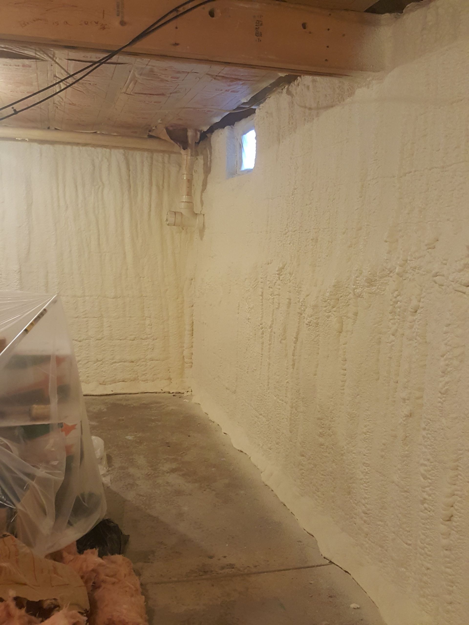 Unfinished basement with white painted walls, exposed ceiling beams, and a concrete floor with plastic-covered items.