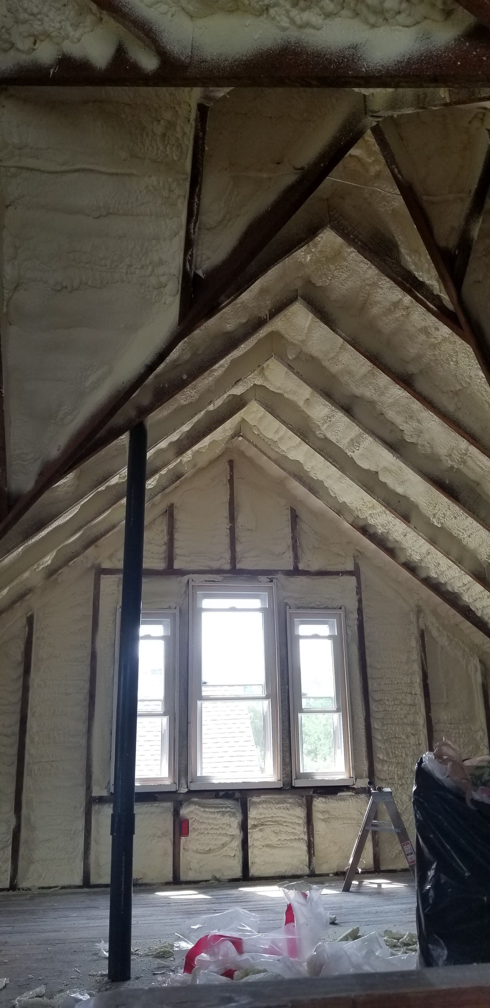 Unfinished attic with exposed insulation and wooden rafters, centered on a small window.