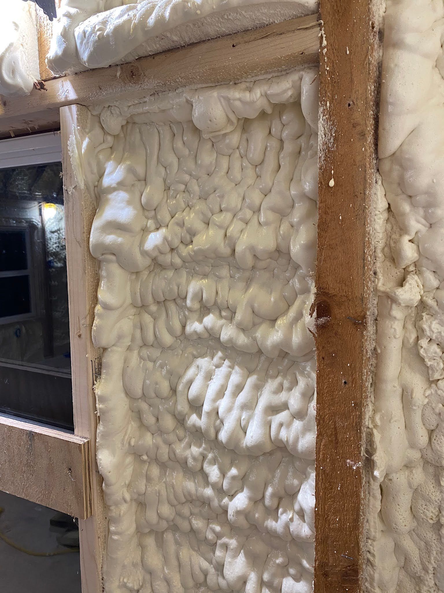 Foam insulation filling a wall cavity beside a rough wooden frame and window opening