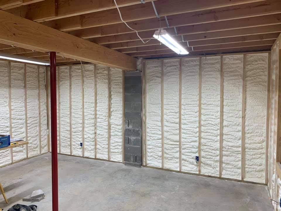Empty unfinished basement with insulated walls, exposed beams, concrete floor, and fluorescent lighting