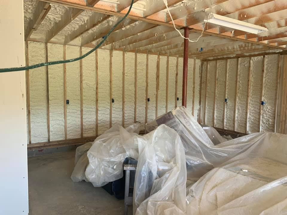 Unfinished garage interior with exposed framing and plastic-covered items on the floor.