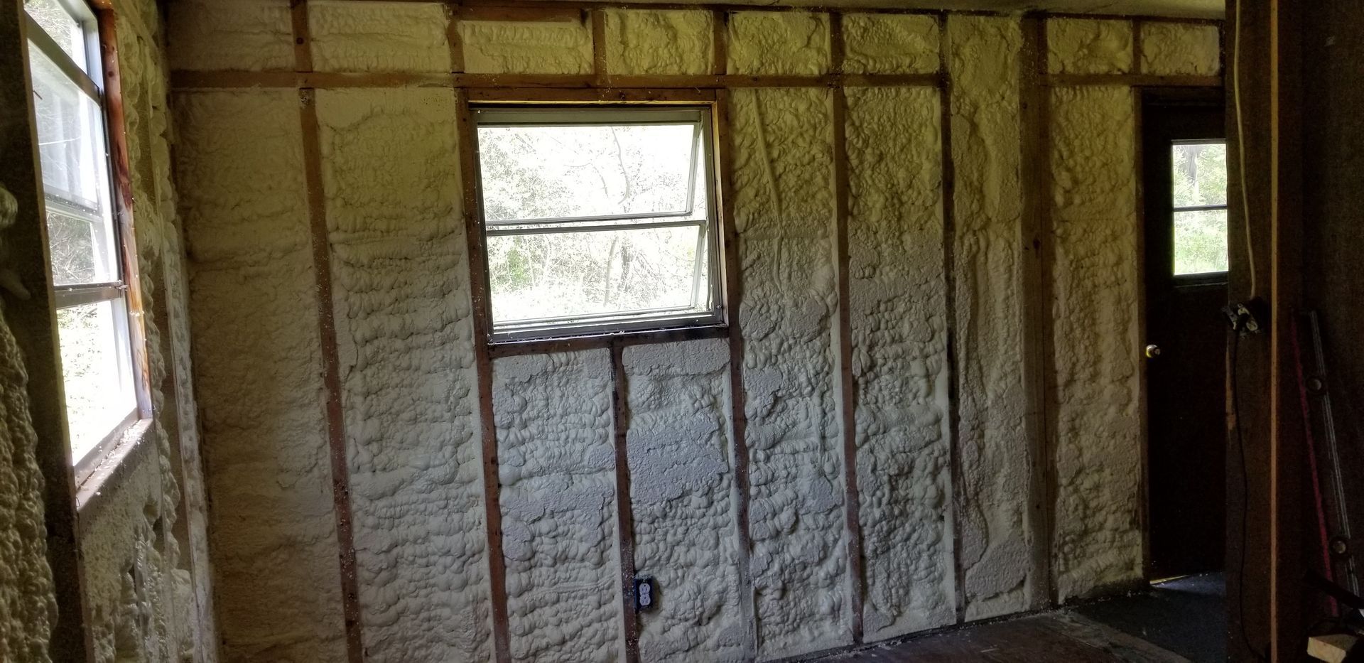 Empty insulated room with exposed wall insulation and two windows allowing daylight in.