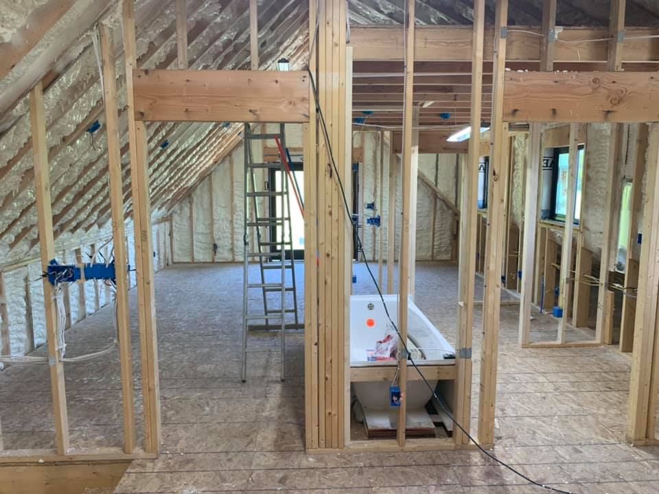 Unfinished attic framing with exposed insulation, studs, and a ladder in a construction space.