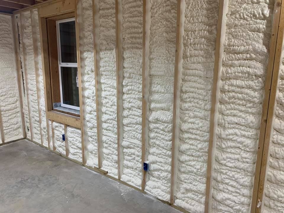 Interior wall with spray foam insulation, a window, and a concrete floor under construction