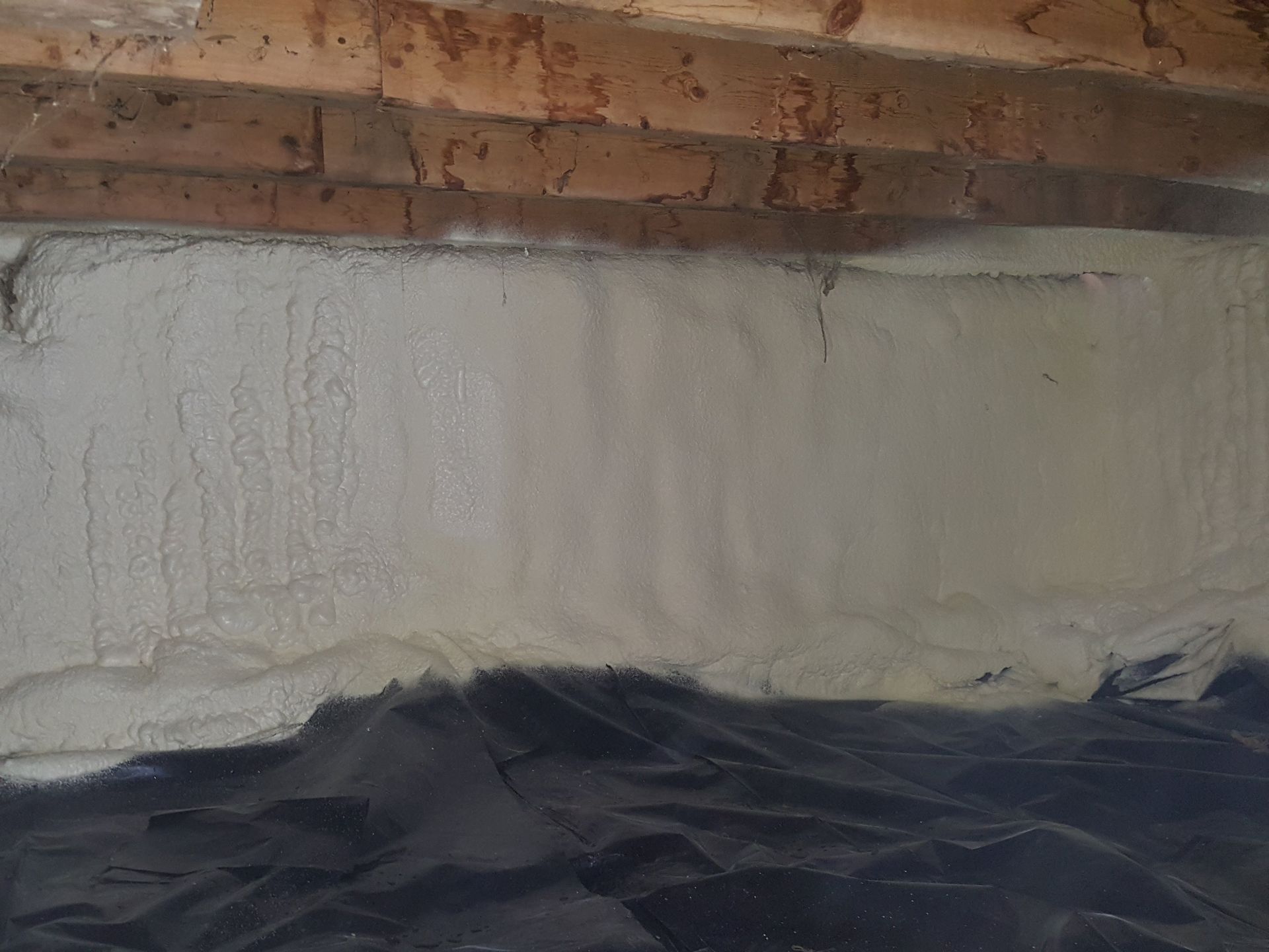 Close-up of a rough white wall under exposed wooden beams and a black tarp covering the floor.