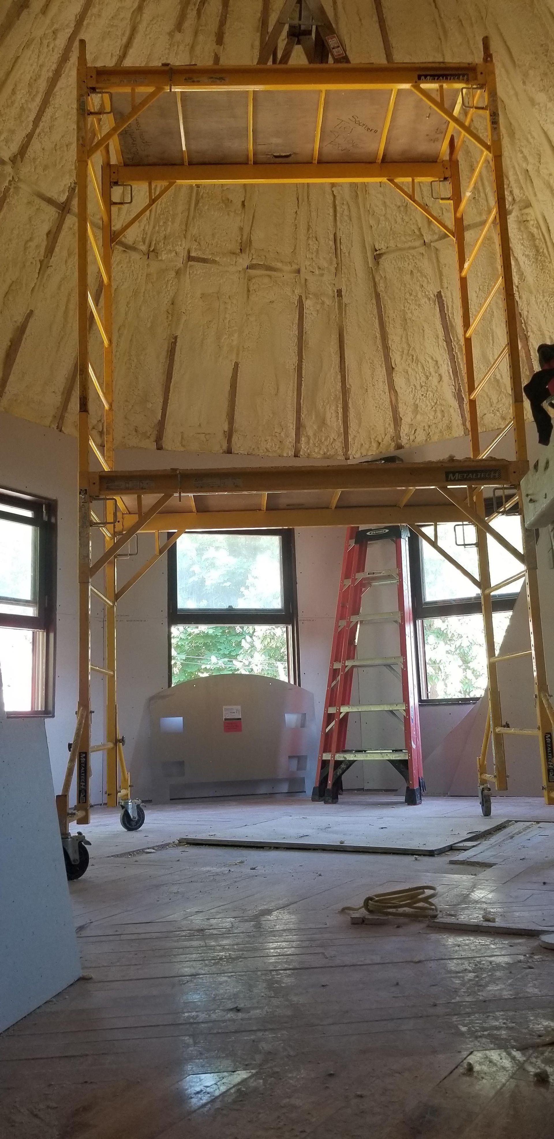 Interior construction site with scaffolding, ladder, exposed walls, and debris on the floor