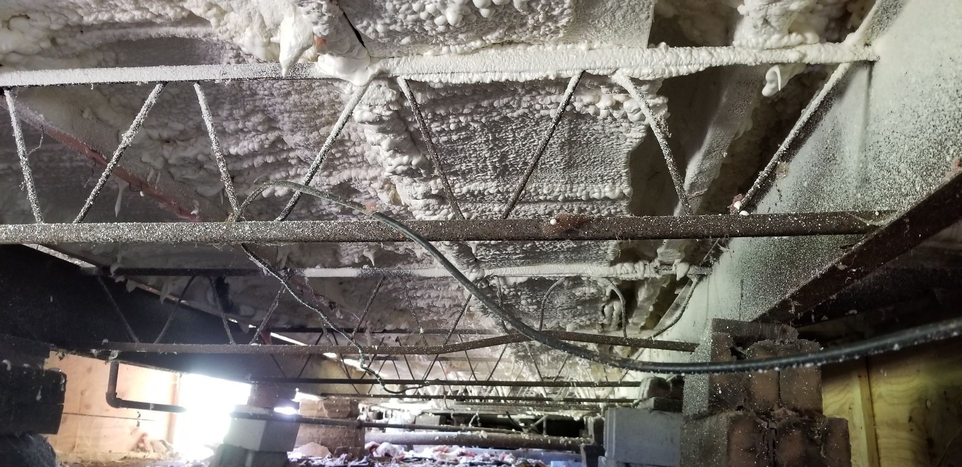 Damaged ceiling with exposed beams and hanging debris in a dimly lit indoor room