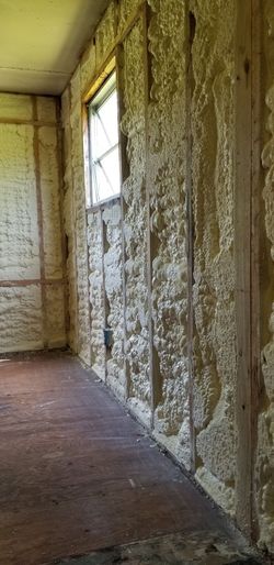 A narrow, unfinished hallway with exposed insulation, a window, and a plywood floor.