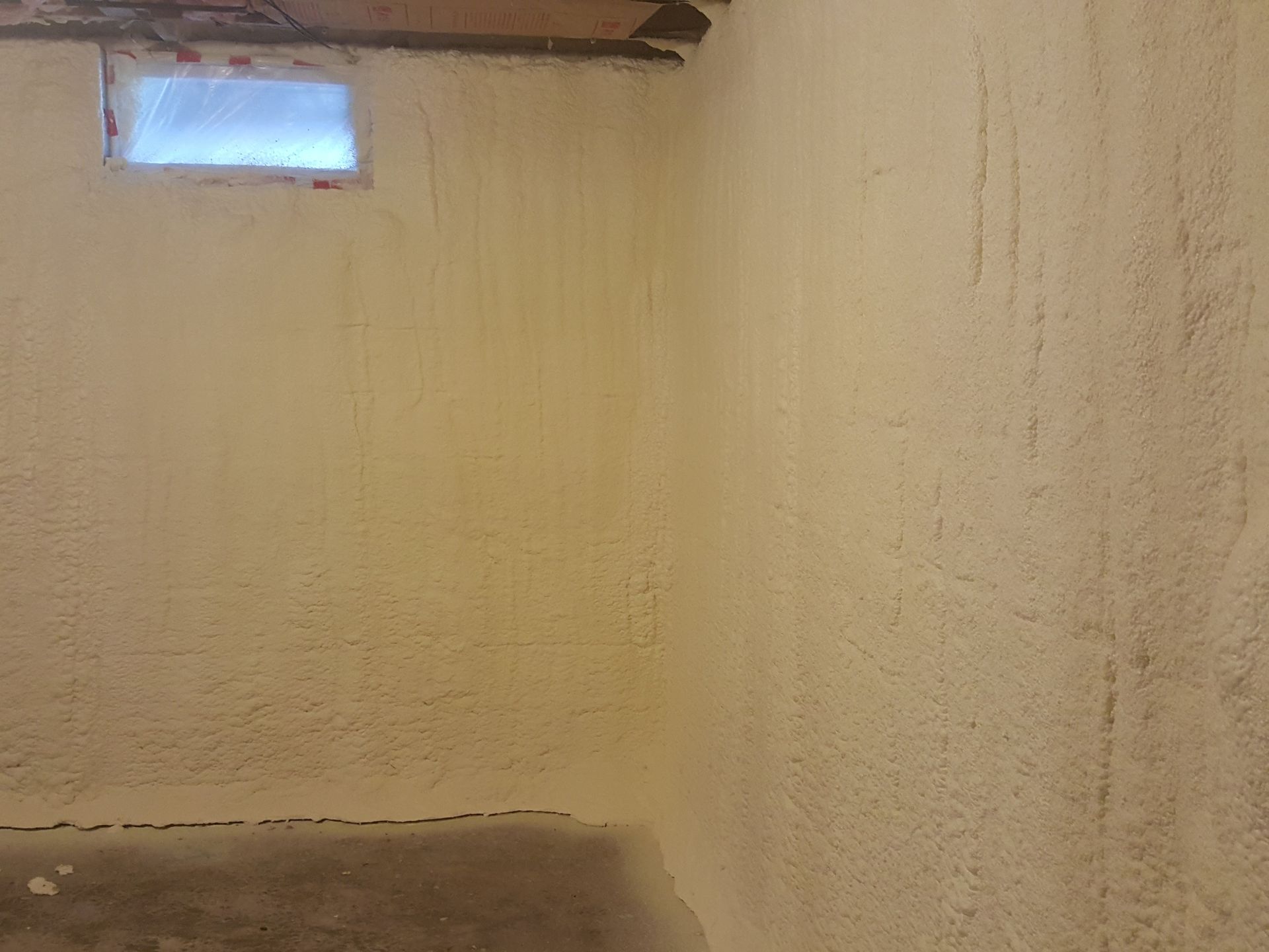 Empty unfinished room with cream walls, a small high window, and bare concrete floor.