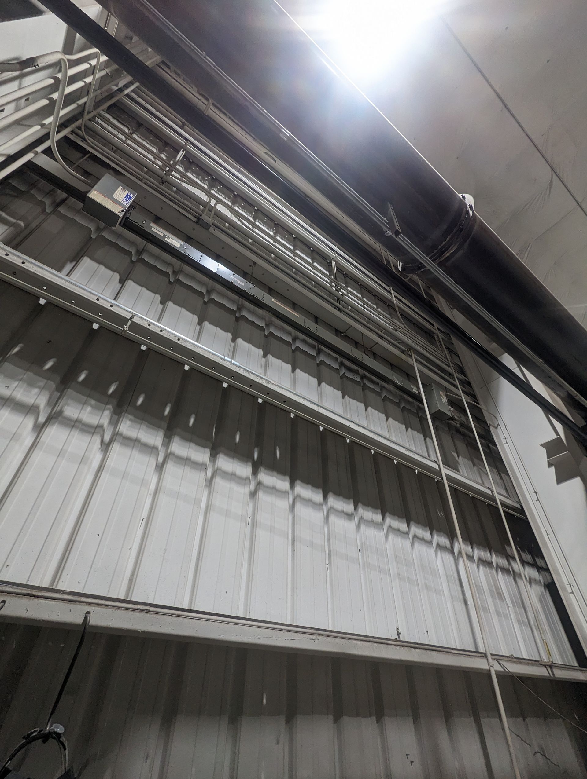 Industrial interior with metal beams, pipes, and a bright ceiling light above corrugated wall panels