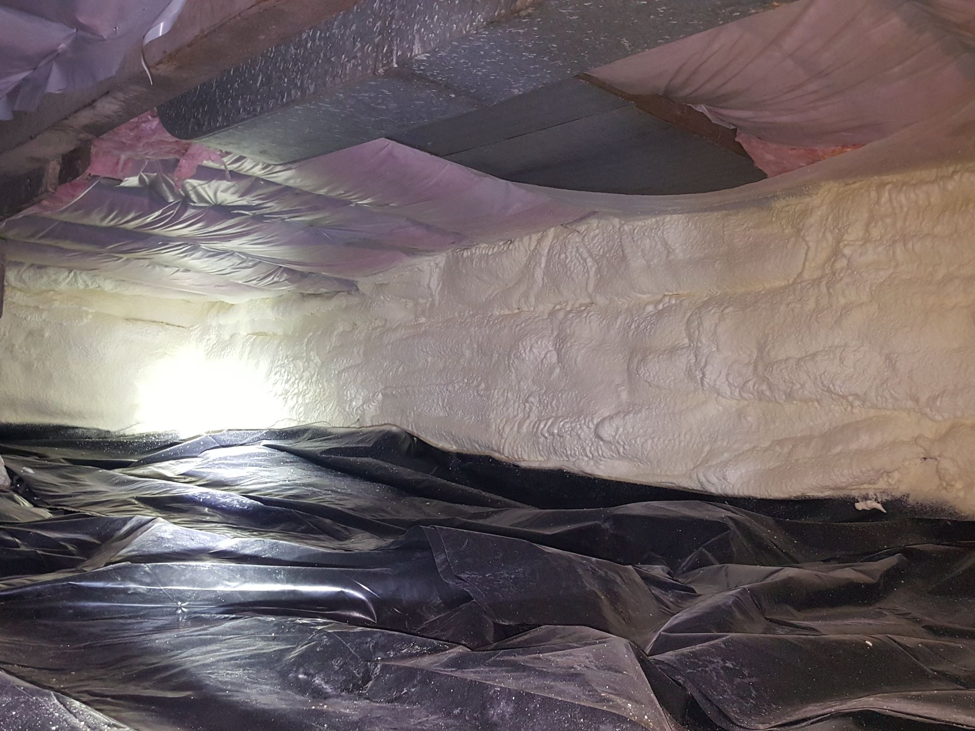 Foil-lined insulation inside an attic or crawlspace with pink and black plastic sheeting